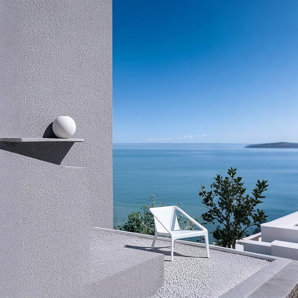 Modern outdoor setting with a white chair and decorative sphere against a blue sea and sky.