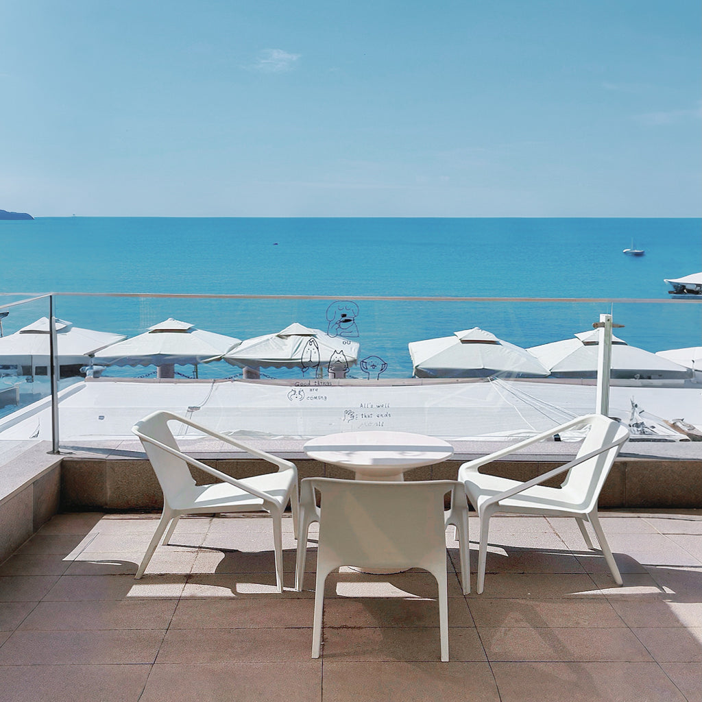 Outdoor seating area with white chairs and table on a balcony overlooking the ocean.